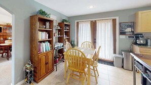 A dining area with a wooden table and chairs, a bookshelf, and a kitchen area with cabinets and appliances. - Springs Sanctuary - Dog-Friendly Home • Decks & Fireplaces (Colorado Springs)