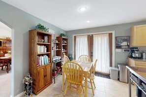 A dining area with a wooden table and chairs, a bookshelf, and a kitchen area with cabinets and appliances. - Springs Sanctuary - Dog-Friendly Home • Decks & Fireplaces (Colorado Springs)