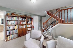 A living room with a staircase, a bookshelf, and two armchairs. - Dog-Friendly 3BR • Two Decks • Fireplaces (Colorado Springs)