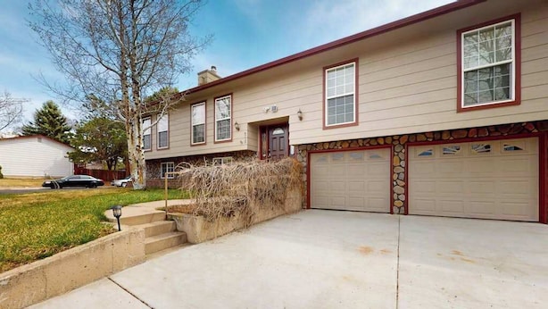 A two-story house with a garage, a front yard with a tree, and a driveway. - Springs Sanctuary - Dog-Friendly Home • Decks & Fireplaces (Colorado Springs)