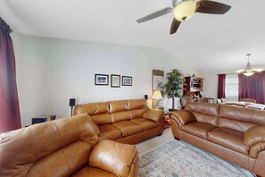 A living room with a brown leather sectional sofa, a ceiling fan, and a dining area in the background. - Dog-Friendly 3BR • Two Decks • Fireplaces (Colorado Springs)