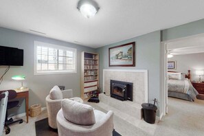 A living room with a fireplace, a bookshelf, a television, and a comfortable seating area. - Dog-Friendly 3BR • Two Decks • Fireplaces (Colorado Springs)