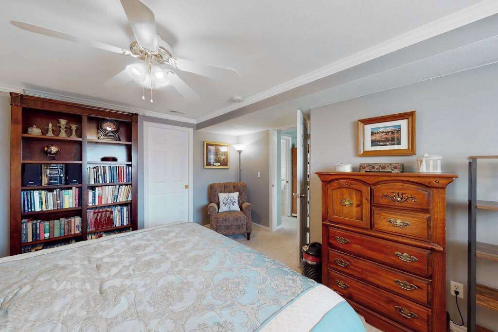 A bedroom with a bed, a ceiling fan, a bookshelf, a dresser, and a chair.