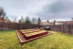 A backyard with raised garden beds, a wooden fence, and a grill. - Dog-Friendly 3BR • Two Decks • Fireplaces (Colorado Springs)