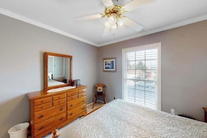 A bedroom with a wooden dresser, a bed with a patterned bedspread, a ceiling fan, a window with blinds, and a framed picture on the wall. - Springs Sanctuary - Dog-Friendly Home • Decks & Fireplaces (Colorado Springs)