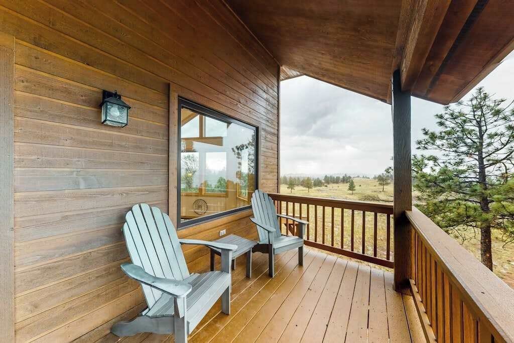 A wooden deck with two Adirondack chairs and a window overlooking a landscape.
