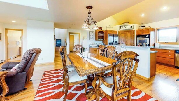 A spacious kitchen with wooden cabinets, a central island, and a dining area with a long table and chairs. - Skyline Ridge - Secluded Retreat • Stunning Views & Loft (Florissant)