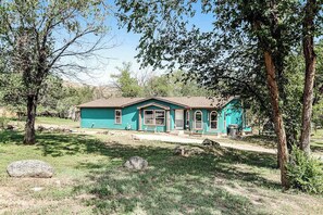 A single-story house with a brown roof and teal siding, surrounded by trees and a grassy yard. - Rocky Mountain Rustic - Mountain-View Home • AC & Fast WiFi (Colorado Springs)