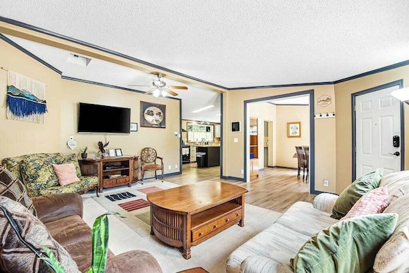 A living room with a sofa, coffee table, and television. There is a kitchen in the background. - Rocky Mountain Rustic - Mountain-View Home • AC & Fast WiFi (Colorado Springs)