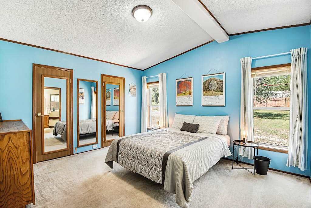 A bedroom with a bed, a dresser, a window with curtains, and a door with a mirror.