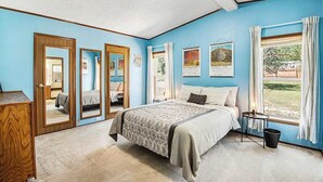A bedroom with a bed, a dresser, a window with curtains, and a door with a mirror. - Rocky Mountain Rustic - Mountain-View Home • AC & Fast WiFi (Colorado Springs)