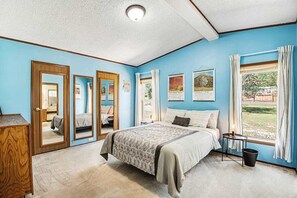 A bedroom with a bed, a dresser, a window with curtains, and a door with a mirror. - Rocky Mountain Rustic - Mountain-View Home • AC & Fast WiFi (Colorado Springs)