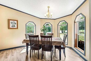 A dining area with a table and chairs, large windows, and a chandelier. - Rocky Mountain Rustic - Mountain-View Home • AC & Fast WiFi (Colorado Springs)