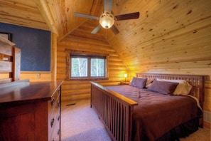 Ein Schlafzimmer in einer Blockhütte mit einem Bett, einem Schreibtisch und einem Fenster.