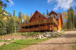 Eine Holzhütte mit Balkon, umgeben von Bäumen und einem Kiesweg.