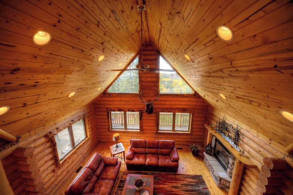 A log cabin interior with a loft bedroom, a fireplace, and a cozy seating area.
