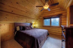 Un dormitorio tipo cabaña de madera con una cama, una ventana, un ventilador de techo y un aparador.