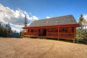 Eine Blockhütte mit Veranda, umgeben von Bäumen und einem klaren Himmel.