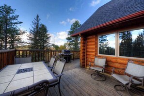 A wooden deck with a table and chairs, a grill, and a cabin with large windows. - Black Diamond Lodge - Log Lodge • Hot Tub & Game Room (Lead)