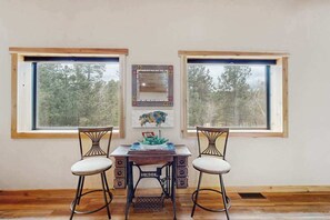 Ein Zimmer mit zwei großen Fenstern, einem Holztisch mit zwei Stühlen und einem an der Wand befestigten Spiegel.