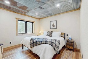 A bedroom with a bed, a bedside table, a window, and a ceiling with a metal grid. - Bear Butte Hideaway - Secluded Hideaway w/ Private Hot Tub (Deadwood)