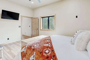 A bedroom with a bed, a television mounted on the wall, a window, and a door. - Bear Butte Hideaway - Secluded Hideaway w/ Private Hot Tub (Deadwood)
