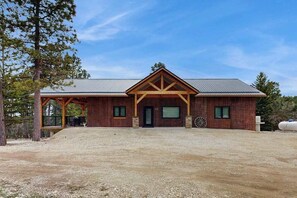 A two-story building with a covered porch, a garage, and a gravel driveway. - Bear Butte Hideaway - Secluded Hideaway w/ Private Hot Tub (Deadwood)
