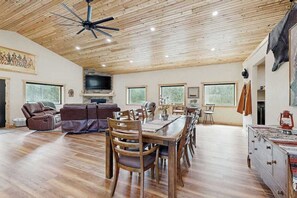 A spacious living area with a wooden ceiling, a dining table with chairs, a sofa, and a television. - Bear Butte Hideaway - Secluded Hideaway w/ Private Hot Tub (Deadwood)