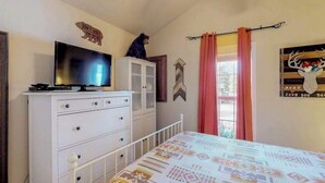Quarto com cama, televisão sobre uma cômoda, decoração de urso e um quadro de veado na parede.
