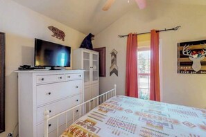 Ein Schlafzimmer mit einem Bett, einem Fernseher auf einer Kommode, einer Bär-Dekoration und einem Wandbild mit einem Hirsch.