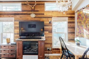 A room with a fireplace, television, and wooden walls. - Cub Cottage - Cozy Tiny Home • Mtn View, Dogs OK (Woodland Park)
