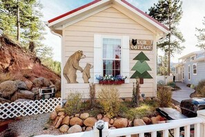 A cottage with a bear and a tree sign, surrounded by rocks and a white fence. - Cub Cottage - Cozy Tiny Home • Mtn View, Dogs OK (Woodland Park)