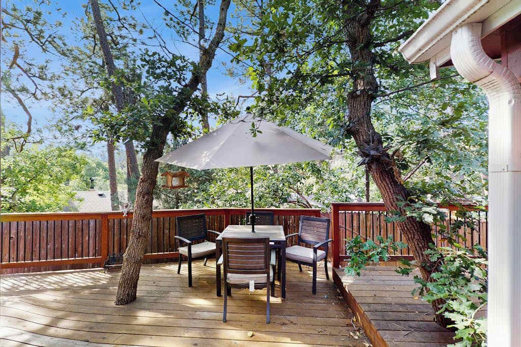 An outdoor deck with a table and chairs, surrounded by trees and a wooden fence.