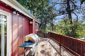 Eine Holzterrasse mit Grill, umgeben von Bäumen und einem roten Gebäude.