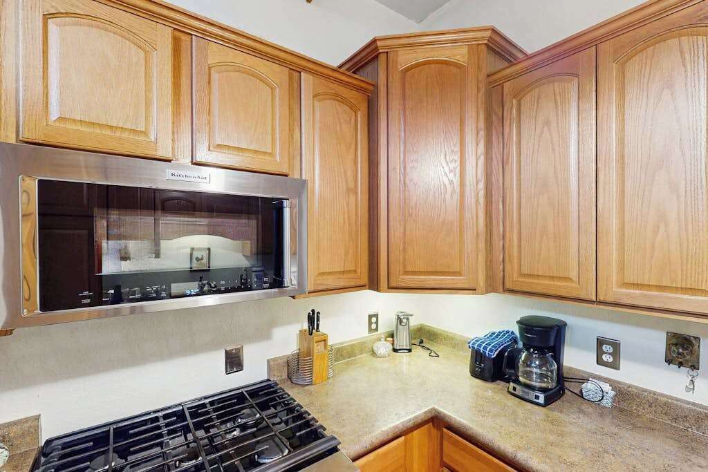 A kitchen with wooden cabinets, a stainless steel range hood, a gas stove, and a coffee maker on the countertop.