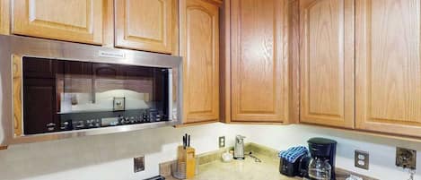 A kitchen with wooden cabinets, a stainless steel range hood, a gas stove, and a coffee maker on the countertop.
