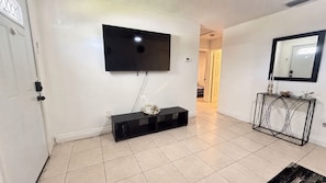 A room with a flat-screen TV mounted on the wall, a black console table with decorative items, and a console with a mirror and candle holders. - Relaxing Melbourne Home Away from Home (Melbourne)