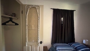 Una habitació amb un llit, una porta amb mosquitera i una cortina fosca.