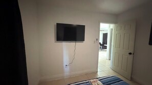 A room with a flat-screen TV mounted on the wall, a door leading to another room, and a striped rug on the floor. - Relaxing Melbourne Home Away from Home (Melbourne)