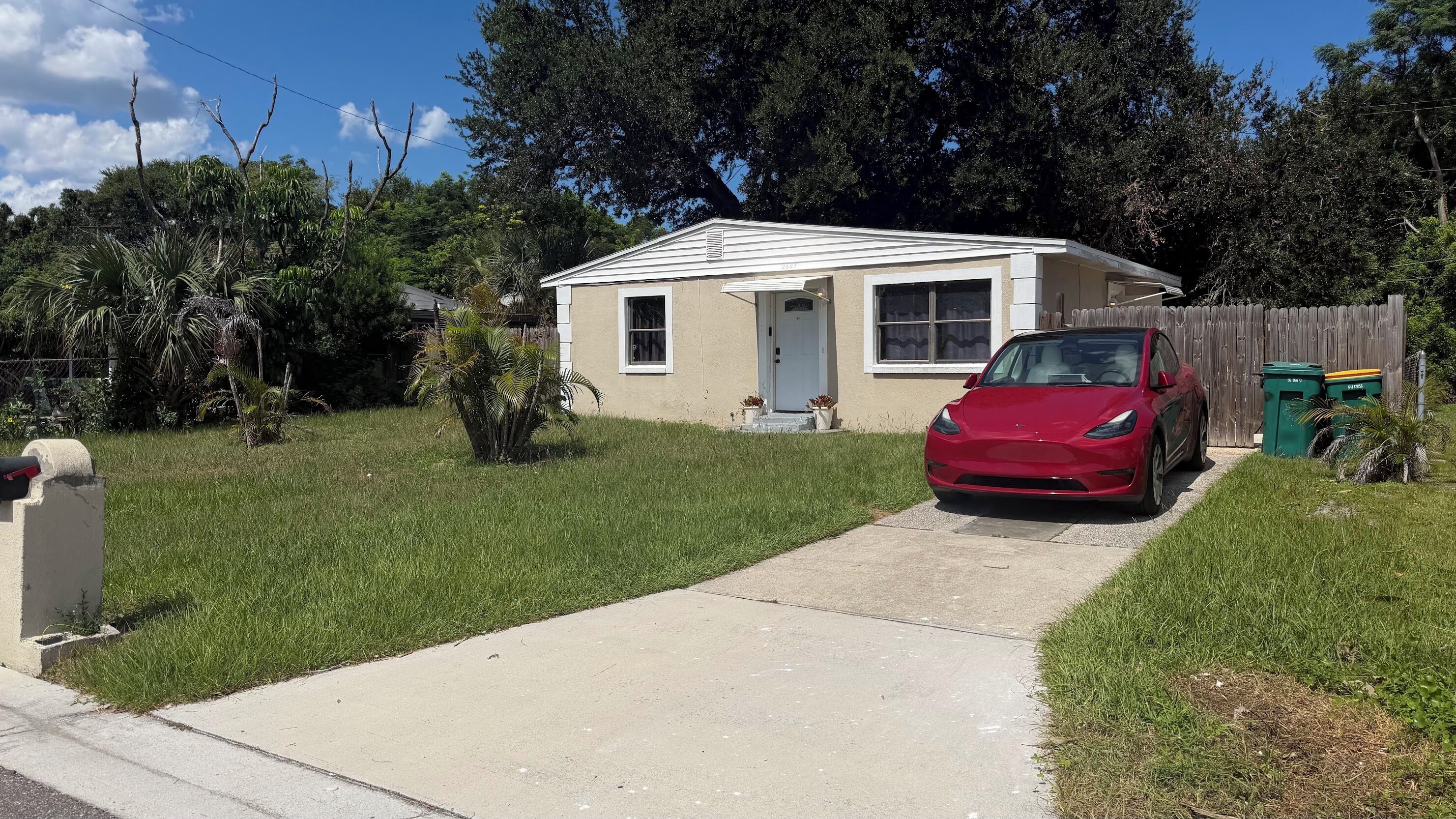 A residential house with a red car parked in the driveway, a front yard with grass, and a wooden fence.