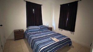 A bedroom with a bed, a nightstand, a dresser, and two windows with curtains. - Relaxing Melbourne Home Away from Home (Melbourne)