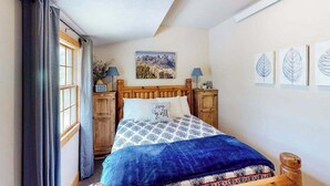 A bedroom with a bed, curtains, a painting, and a lamp. - Mountain View Escape - Dog-Friendly Cabin • Amazing Views (Lead)