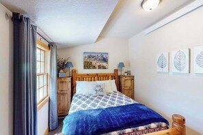 Ein Schlafzimmer mit einem Bett, Vorhängen, einem Gemälde und einer Lampe.