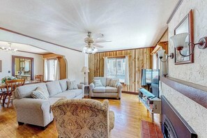 A spacious living room with a wooden floor, a ceiling fan, and a fireplace. - Miners Cottage - Cozy Cottage • Fireplace Near Deadwood (Lead)
