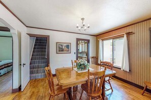 A dining area with a wooden table and chairs, a chandelier, and a staircase leading to another room. - Miners Cottage - Cozy Cottage • Fireplace Near Deadwood (Lead)