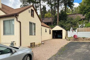 A residential building with a garage, a gravel driveway, and a parked car. - Miners Cottage - Cozy Cottage • Fireplace Near Deadwood (Lead)