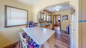 A kitchen with a central island, white cabinetry, and a window with blinds. - Miners Cottage - Cozy Cottage • Fireplace Near Deadwood (Lead)