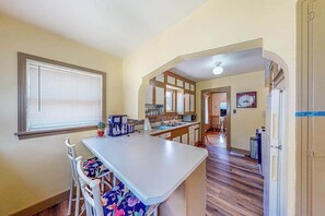 A kitchen with a central island, white cabinetry, and a window with blinds. - Miners Cottage - Cozy Cottage • Fireplace Near Deadwood (Lead)