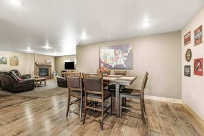 A spacious living room with a fireplace, a dining area with wooden chairs, and a wall with various decorations. - Klassy Lodge - Private Hot Tub & Game Room (Sturgis)