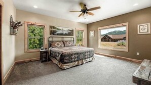 Ein Schlafzimmer mit einem Bett, einem Deckenventilator, zwei Fenstern und Blick auf ein Haus.